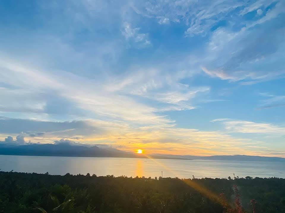 Vivid golden sunset over the calm sea horizon with sun rays reflecting onto the water and dramatic blue sky over Southern Cebu