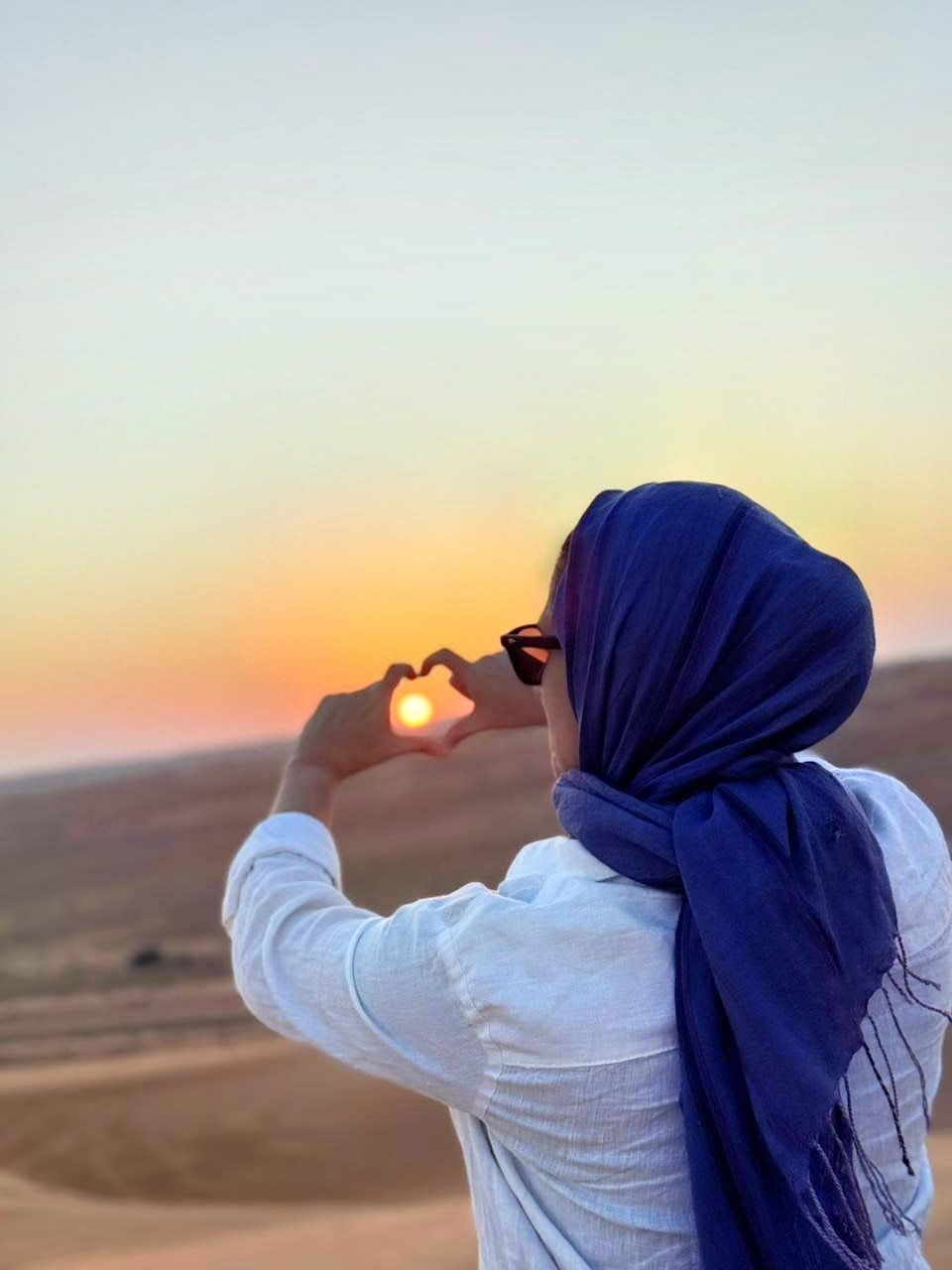 Guest framing the golden desert sunset with heart hands