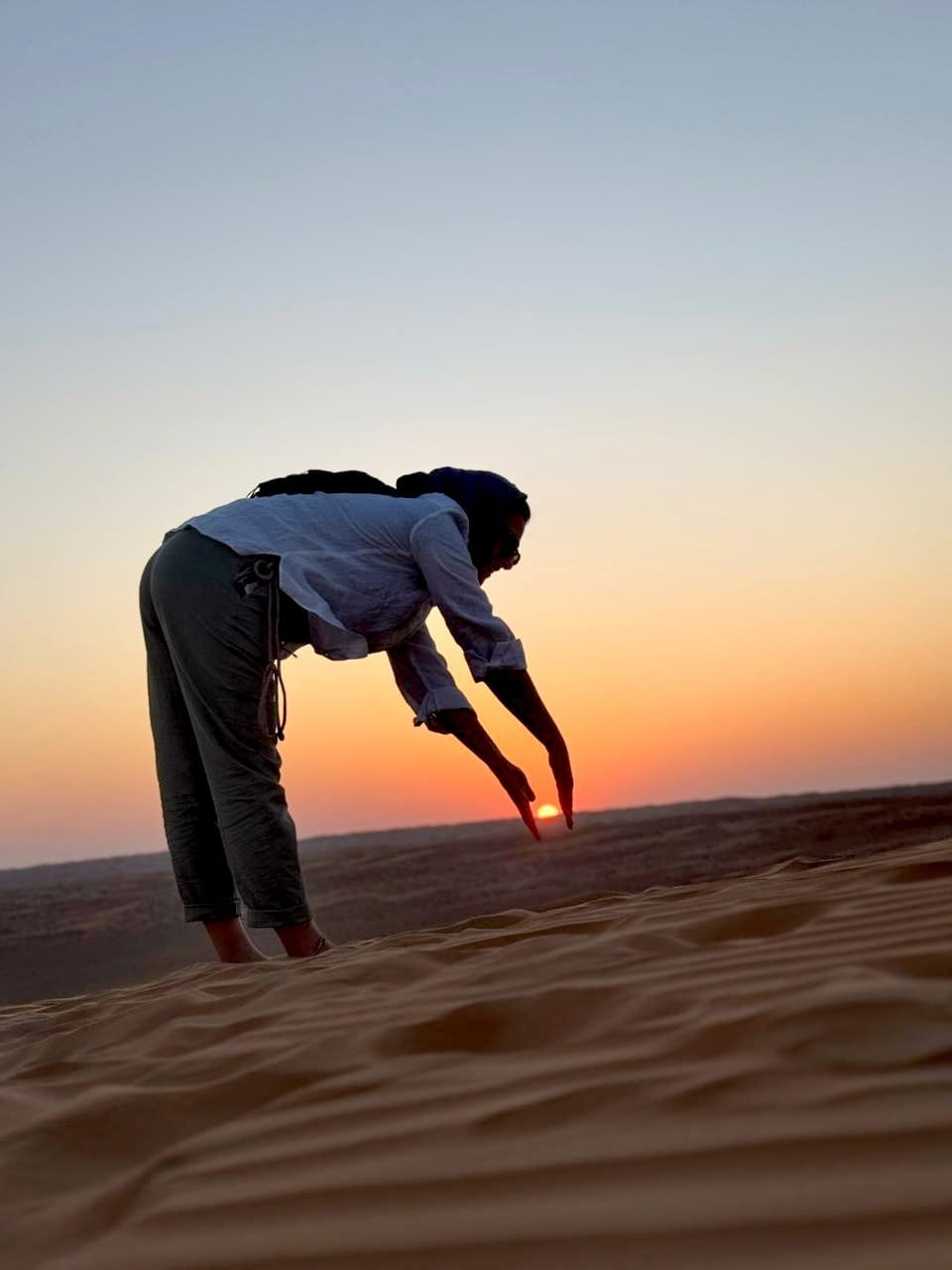 Playful silhouette photo touching the setting sun on top of the dune