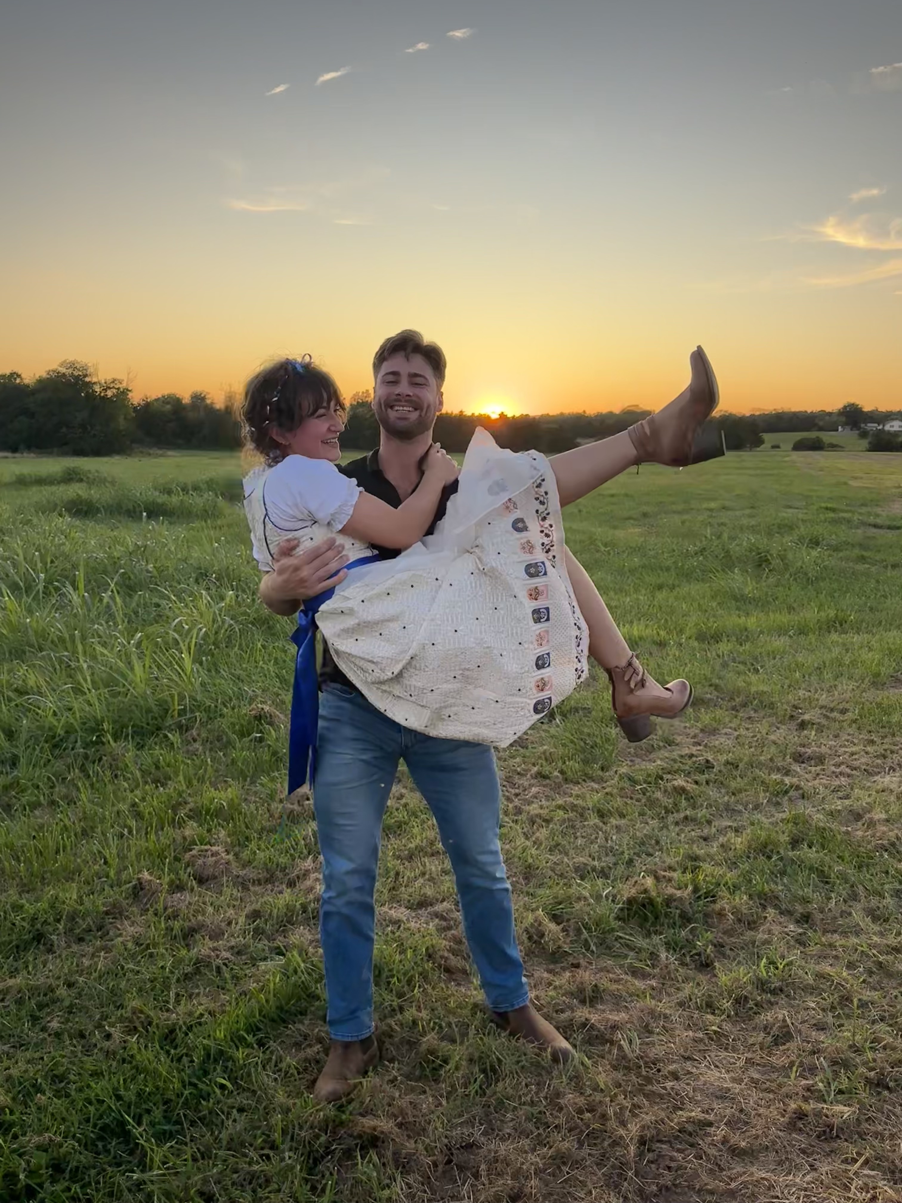 Jacob smiling while holding a woman outdoors at sunset.