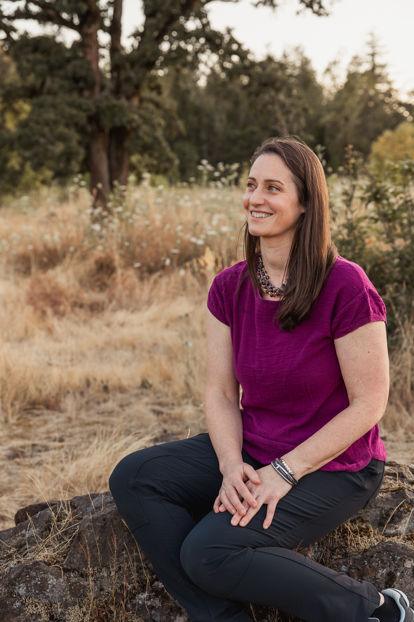Dr. Stefanie Krupp sitting outdoors on a rock in natural sunlight, smiling candidly