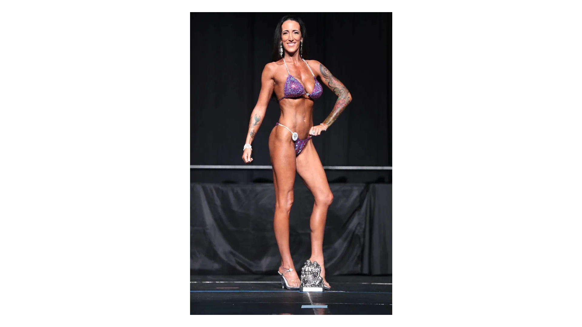 Bikini competitor posing with trophy on stage