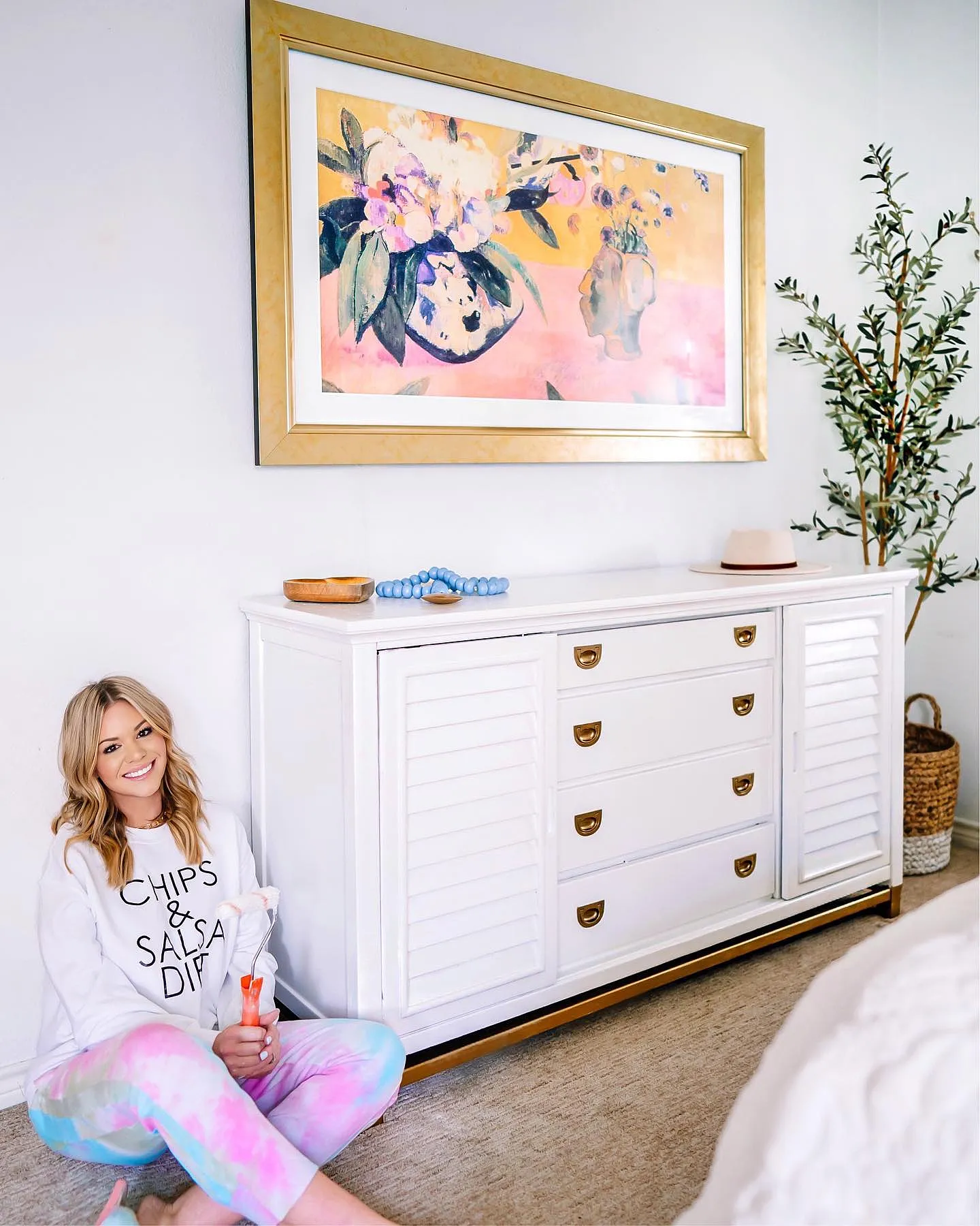 Bright sunlit room featuring an antique gold framed Samsung Frame TV displaying vibrant floral oil painting above a white credenza.