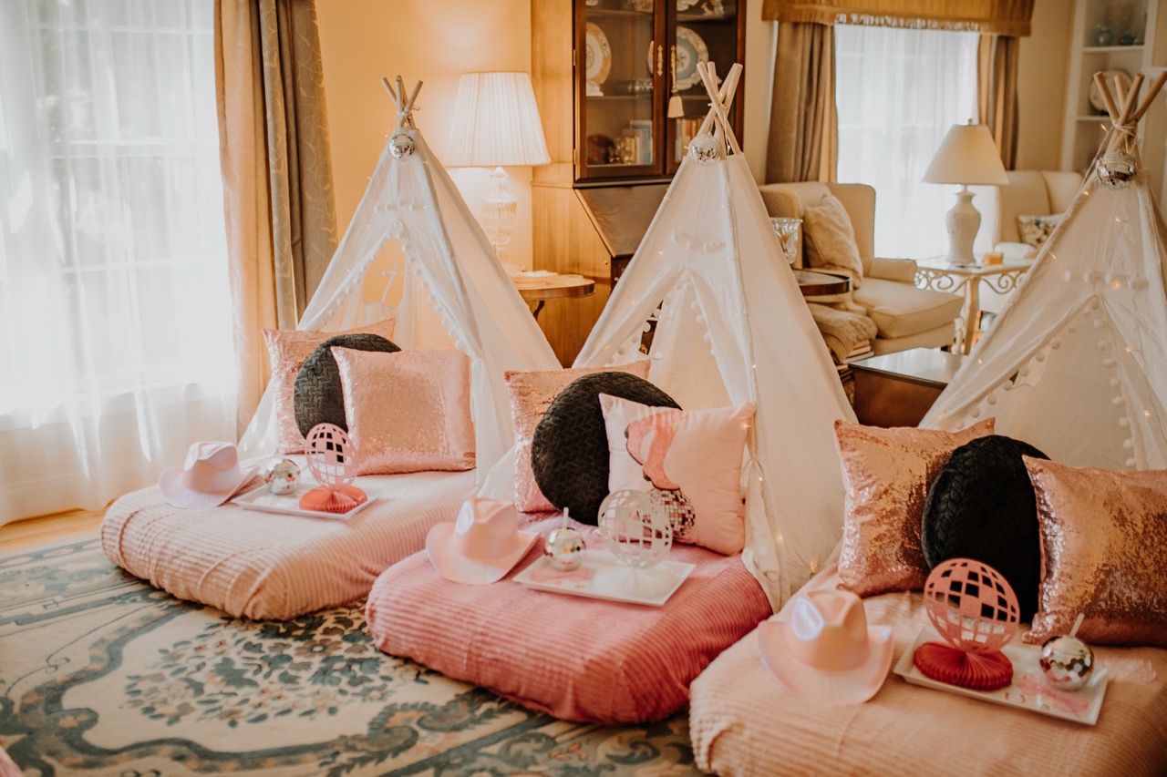 Three white canvas teepees lined up with pink corduroy mattresses and personalized trays