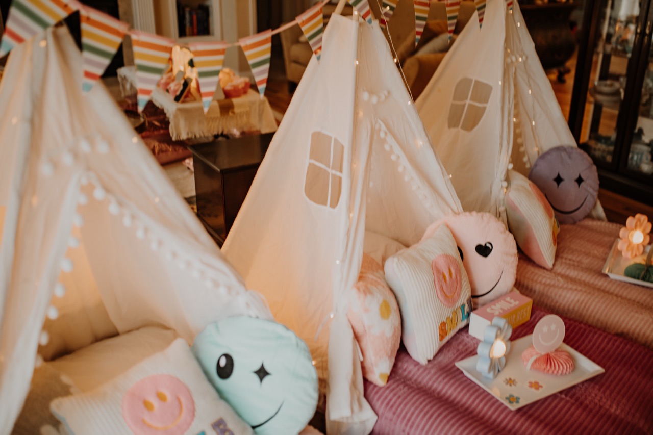 Three white canvas teepees styled in the Flower Power theme with fairy lights and spa setup in background