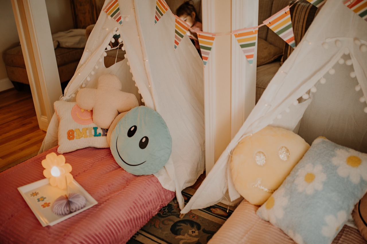 Close-up of cozy Flower Power teepee setup with smiley plush, daisy pillow, and lit flower lamp