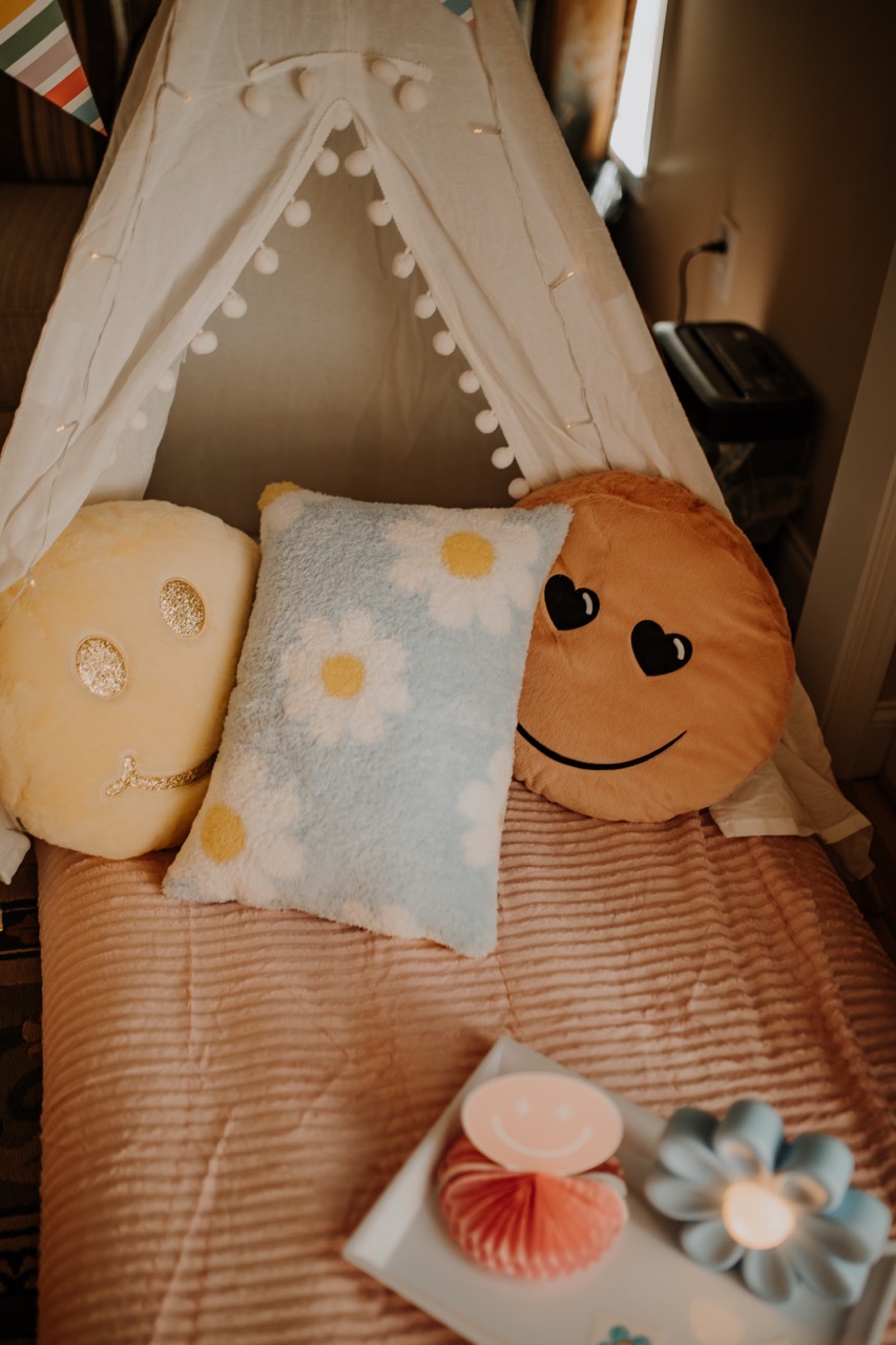 Plush daisy and smiley cushions on pink corduroy bedding inside styled teepee