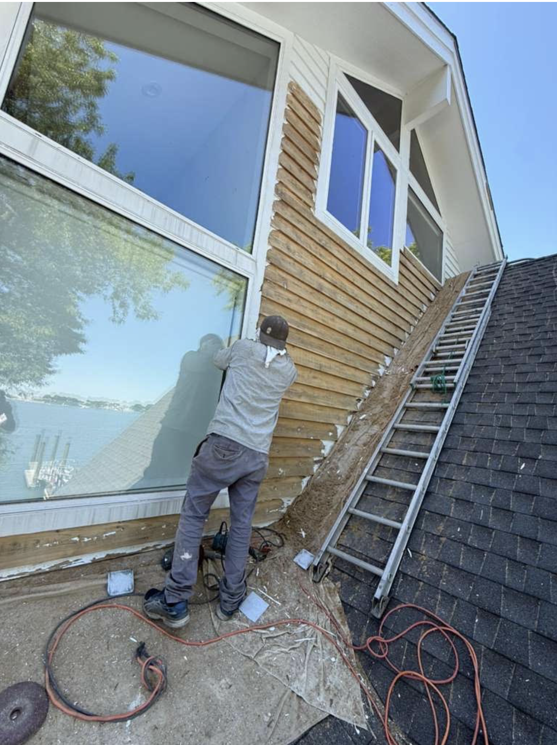 Walter hand-sanding weathered cedar clapboard on roofline
