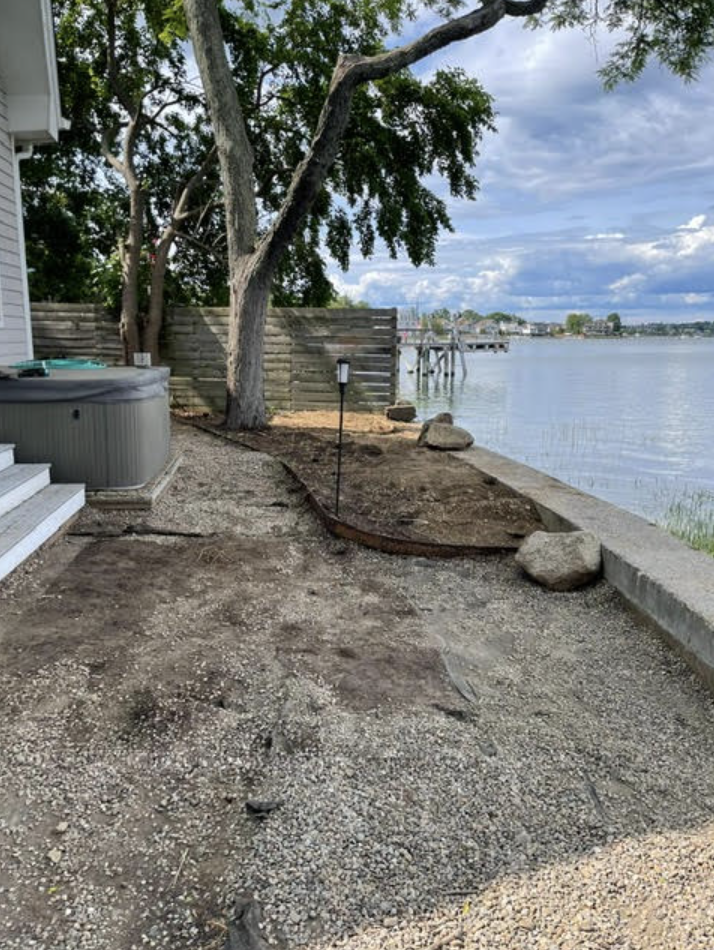 Backyard overlooking water before renovation: old hot tub, gravel, and unkempt soil