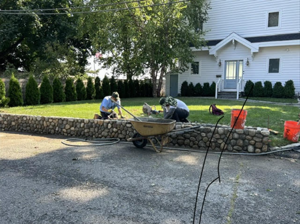 Masons building custom natural stone retaining wall along the front driveway and lawn border