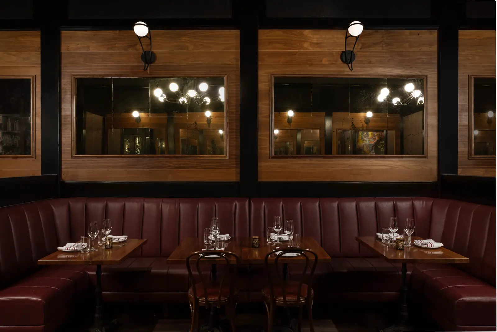 Et Voilà French Bistro private burgundy leather booth and wood tables set with wine glasses under warm sconces in San Diego