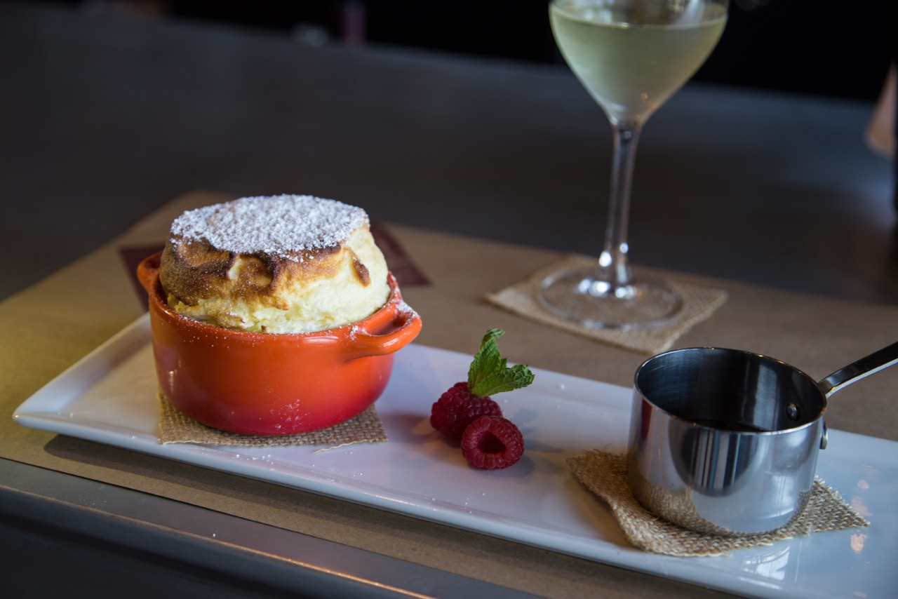 Freshly baked authentic French Soufflé du Jour dusted with powdered sugar in orange ramekin at Et Voilà French Bistro San Diego