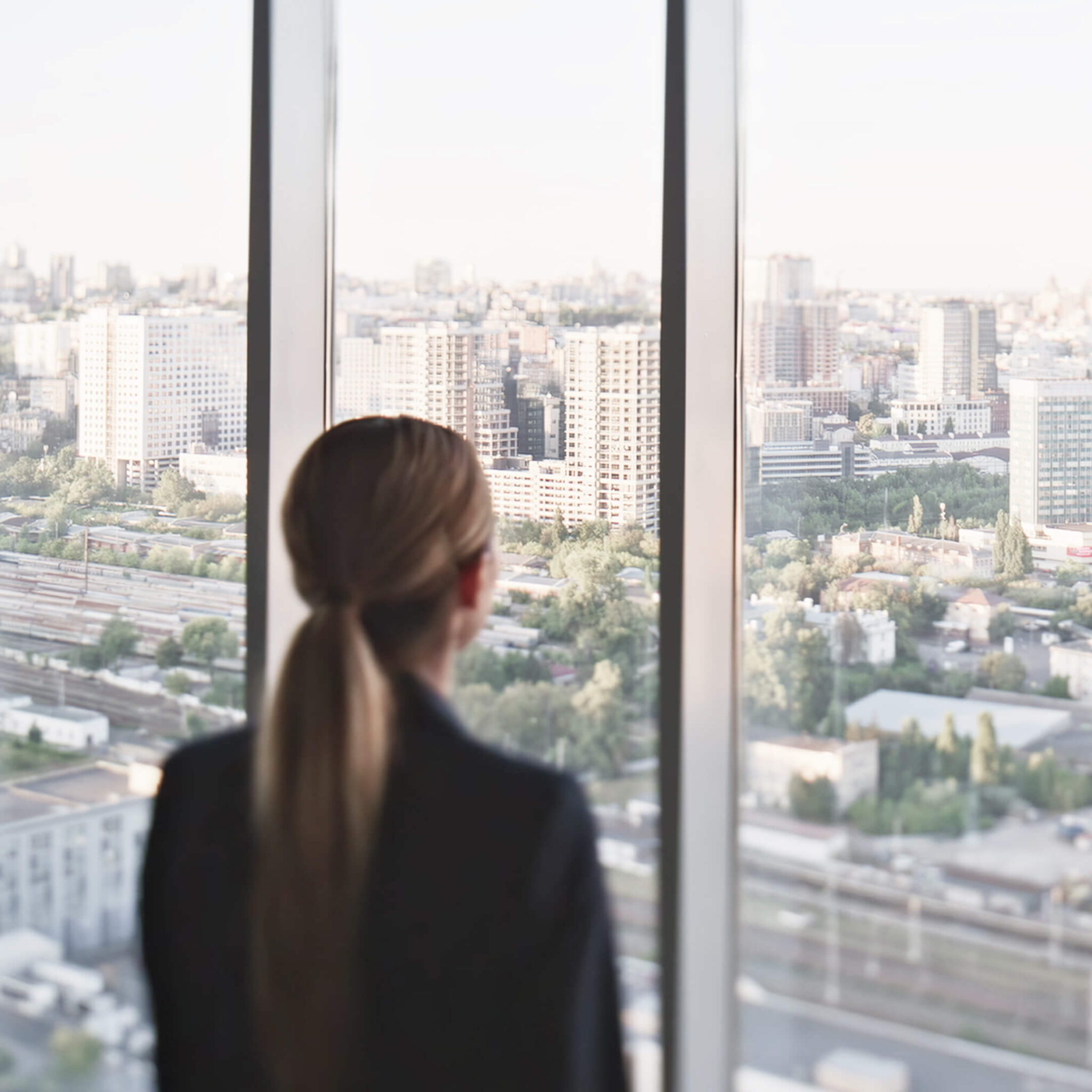 Professional looking out high-rise office window over city horizon