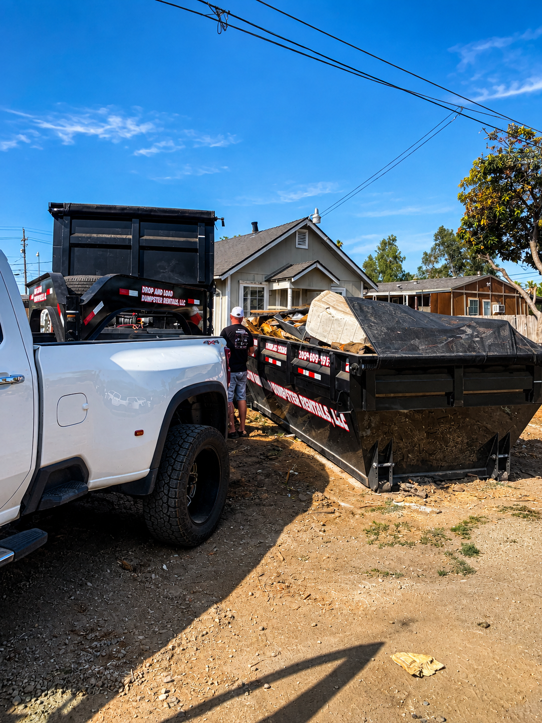 Drop And Load truck and loaded roll-off dumpster at residential cleanout jobsite