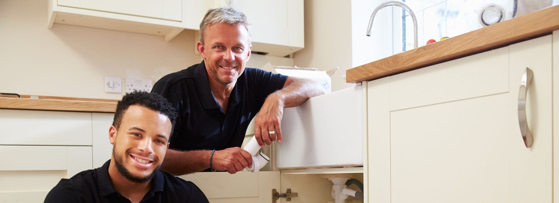 Plumbers performing repair work beneath a sink
