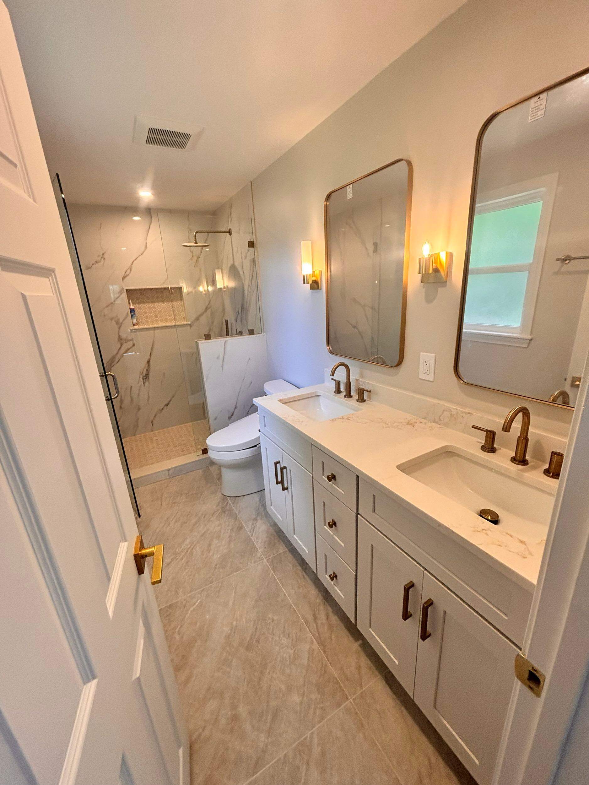 Completed luxury bathroom remodel with double vanity, gold brass fixtures, and walk in marble tile shower