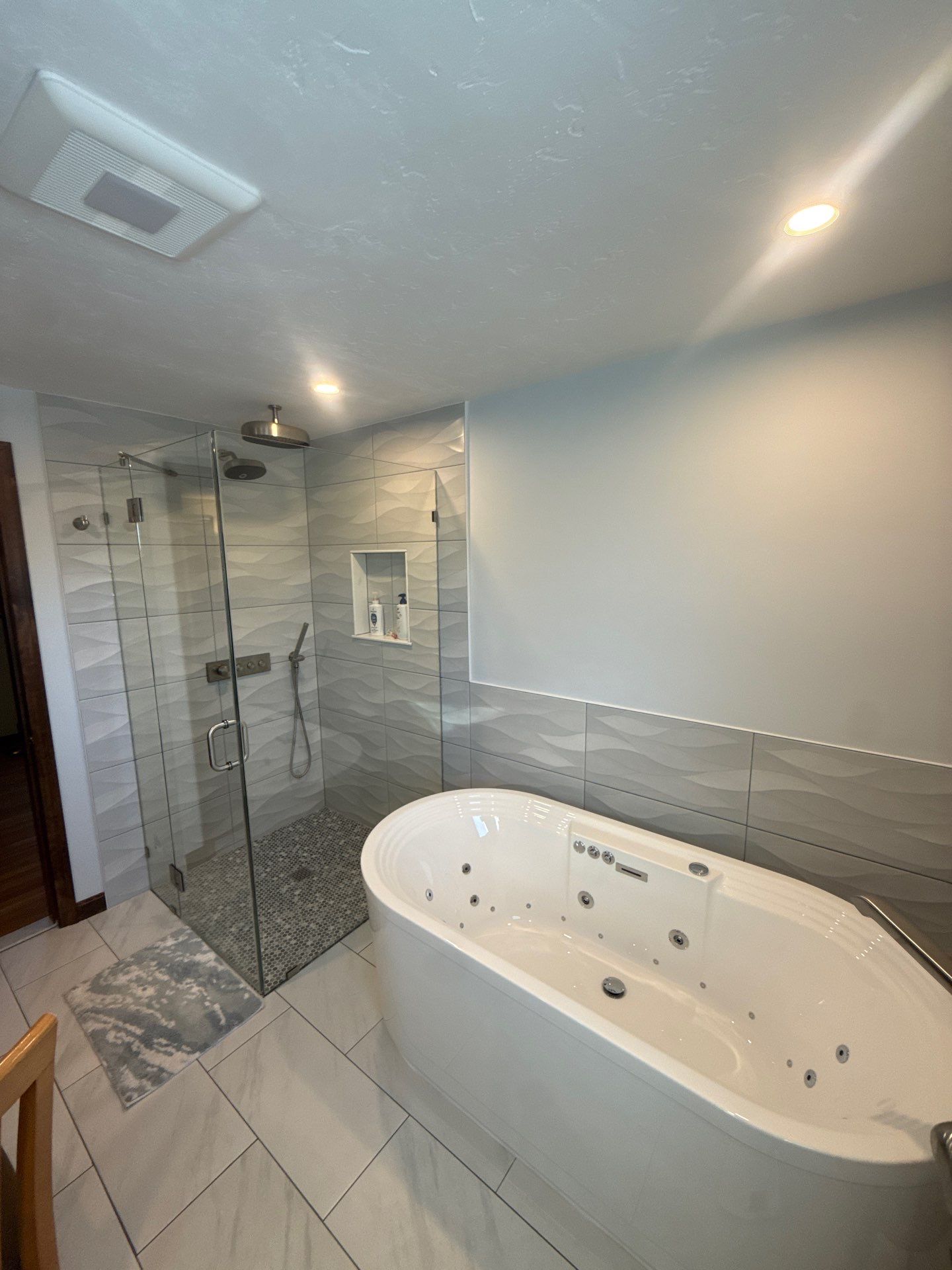 Completed luxury bathroom with freestanding jetted soaking tub and frameless glass walk in shower with textured wall tile