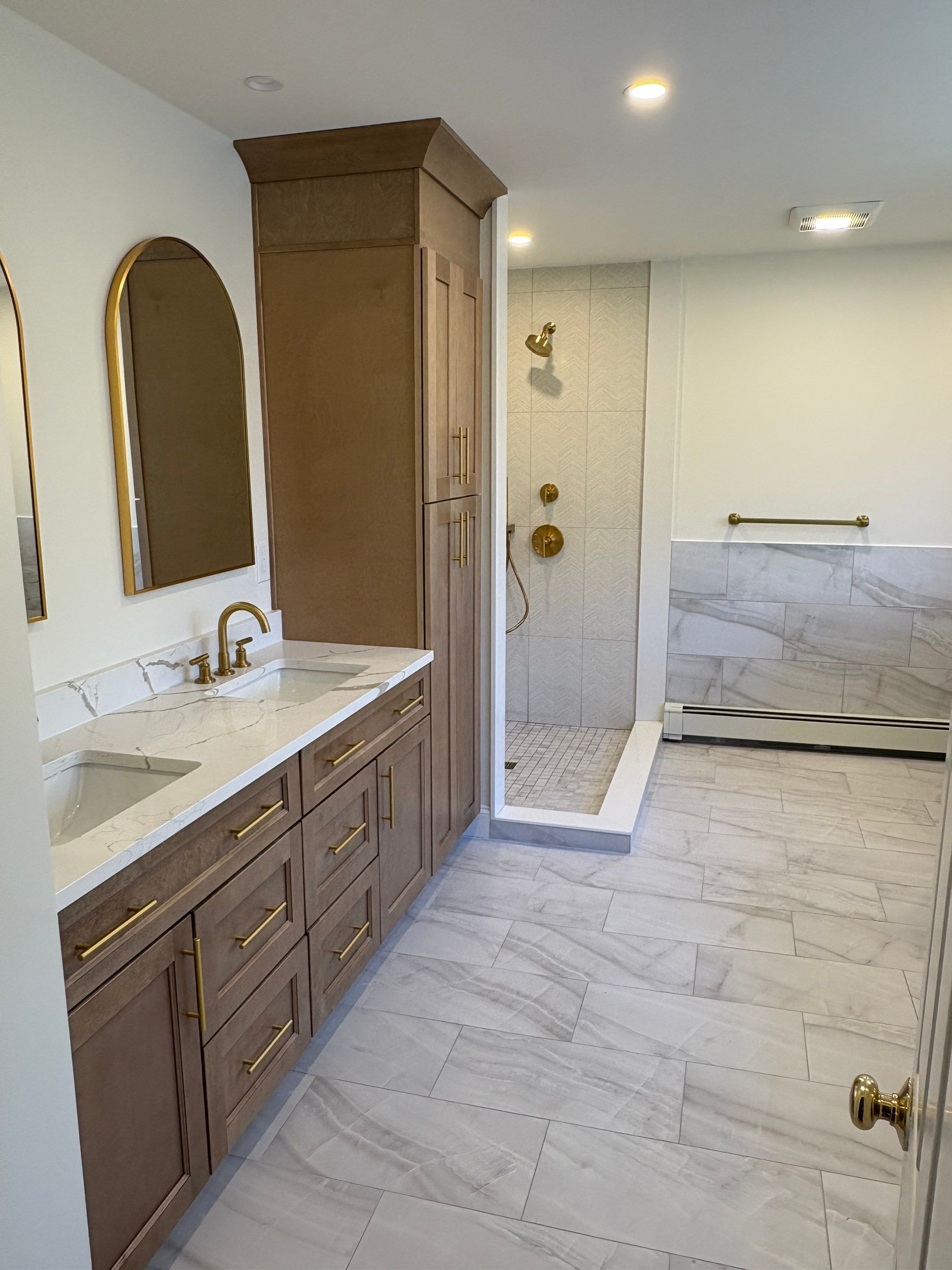 Completed master bathroom with custom wood linen tower, quartz double vanity, brass faucets, and walk in shower