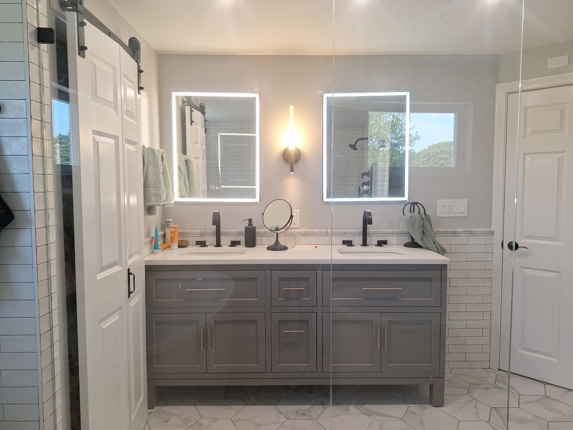 After remodel: grey double vanity with quartz top, dual LED backlit mirrors, black faucets, and hex tile