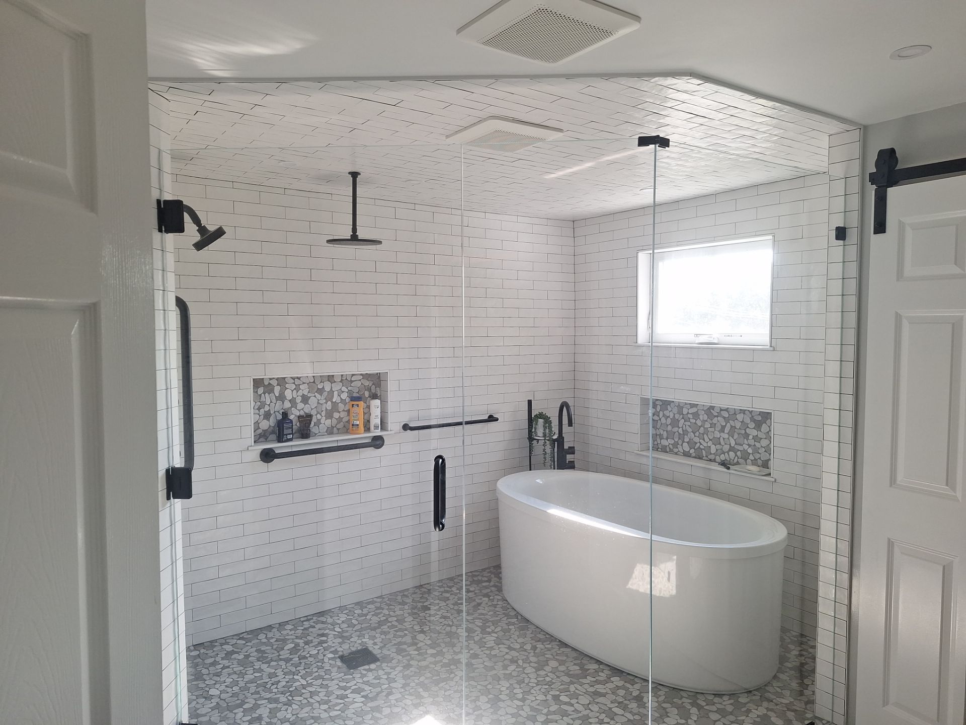 After remodel: modern wet room with freestanding soaking tub, pebble floor, subway tile, and frameless glass