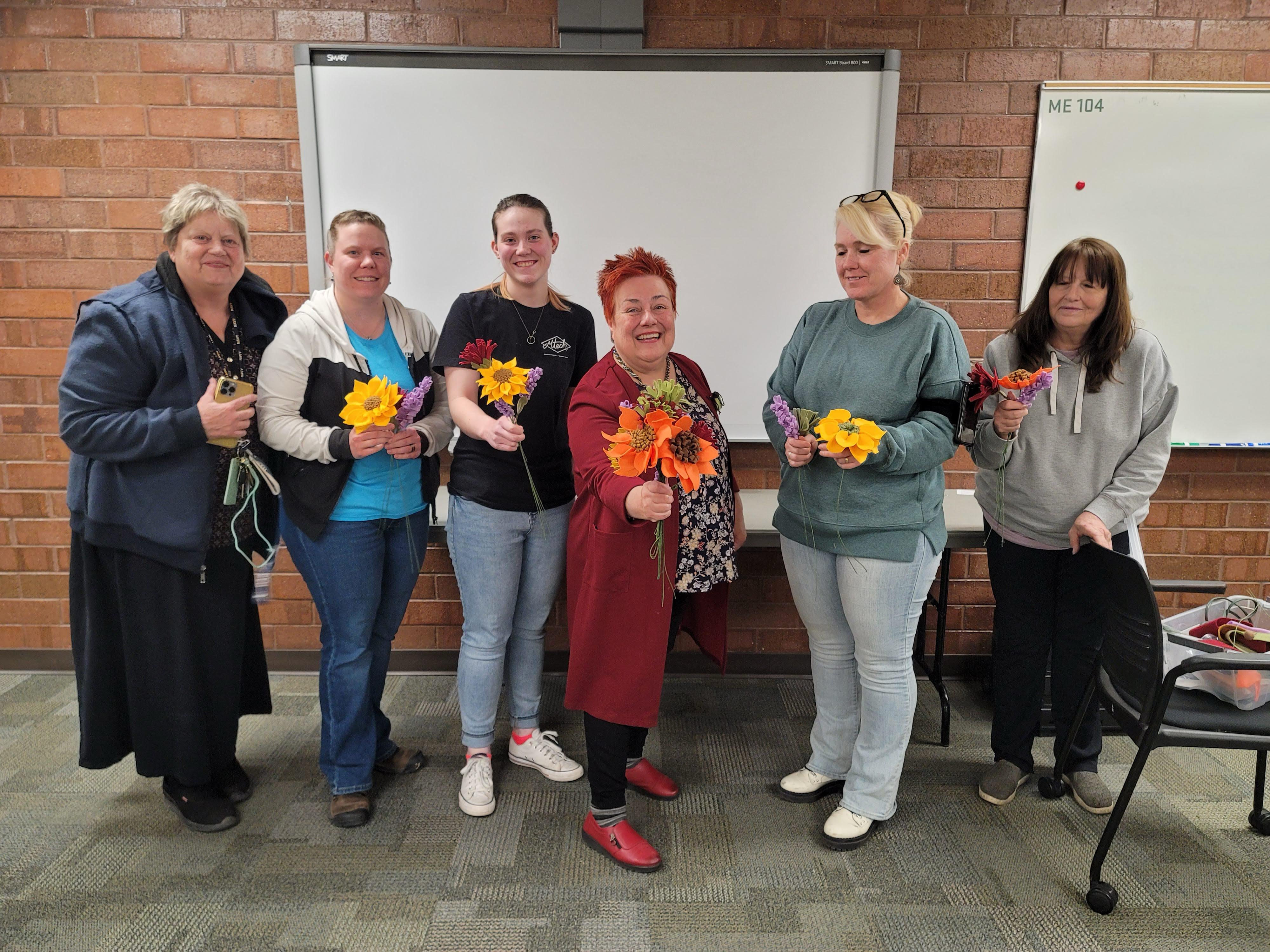 Group of smiling women holding colorful handcrafted felt sunflower and autumn blossom bouquets