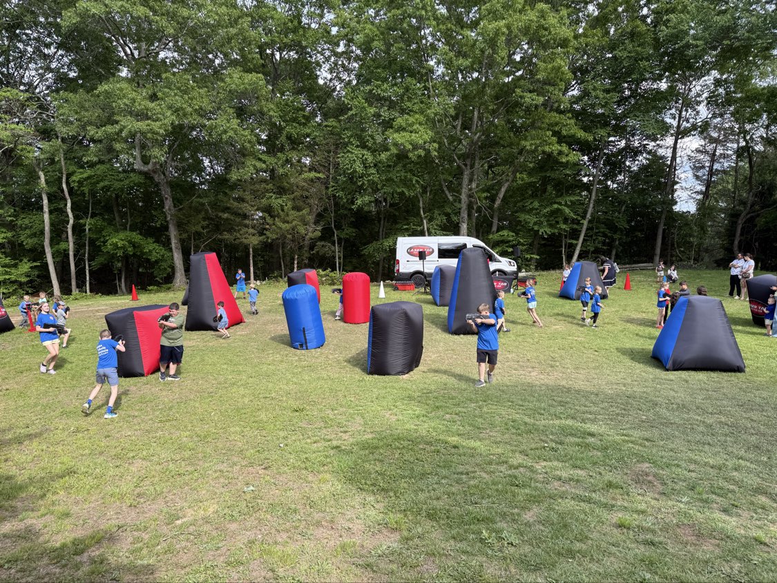 Outdoor field setup for a laser tag birthday party with mobile van and inflatable bunkers