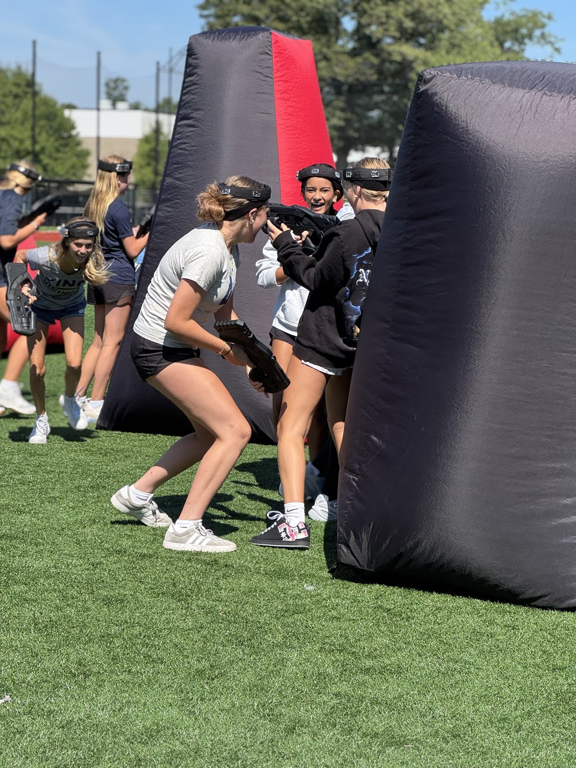 Students actively playing laser tag on an outdoor turf field around inflatable bunkers