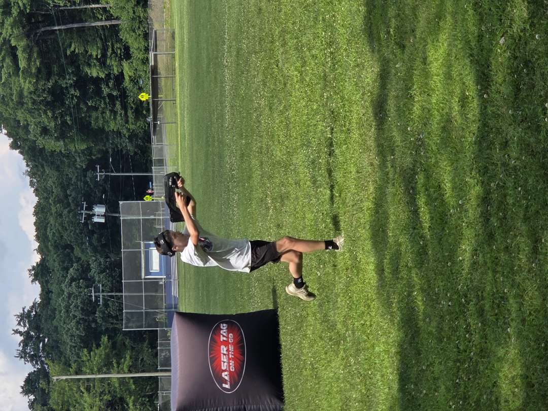 Young camper taking aim with a mobile laser tag blaster on an athletic camp field