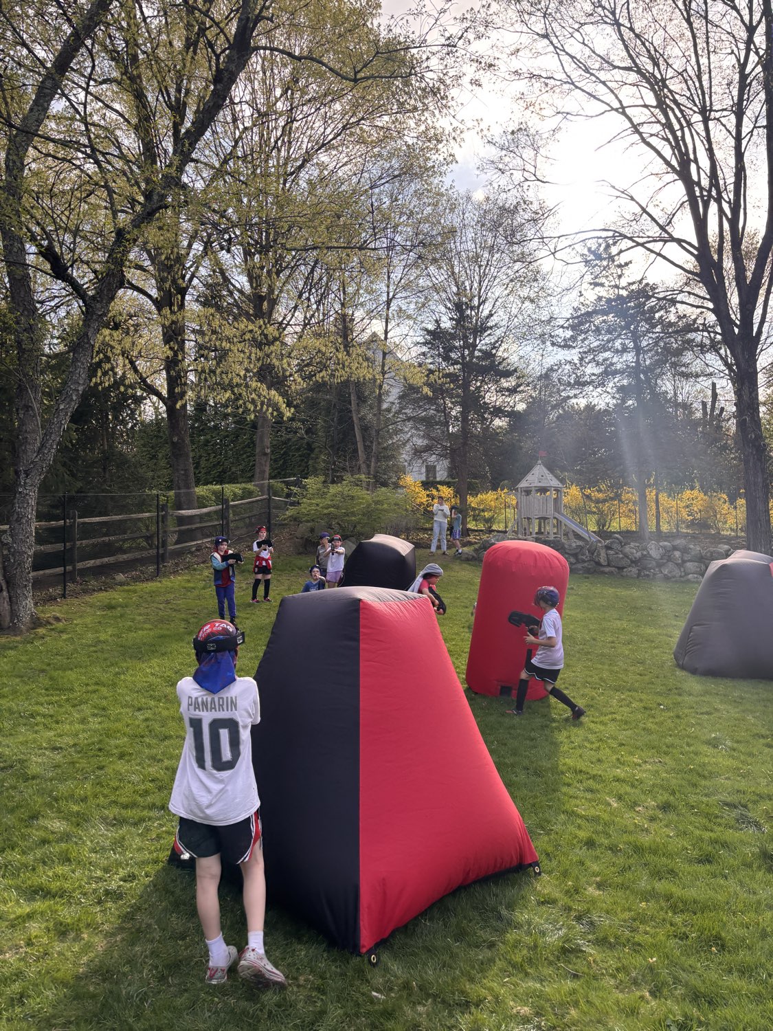 Players navigating around red and black inflatable bunkers during a backyard birthday laser tag party