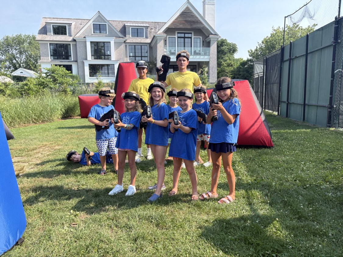 Summer camp kids and Game Coaches posing with blasters and headbands in front of red mobile laser tag bunkers