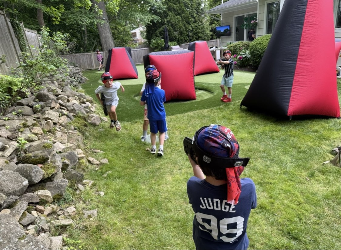 Kids actively playing mobile laser tag in a backyard setup with red and black inflatable bunkers