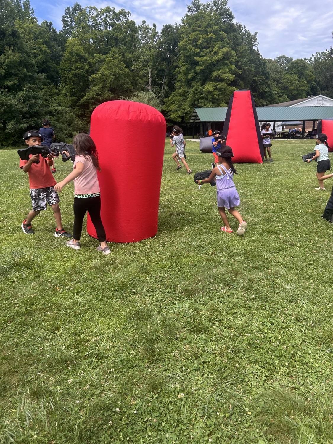 Summer camp kids running and tagging around large red inflatable bunkers during an outdoor laser tag event