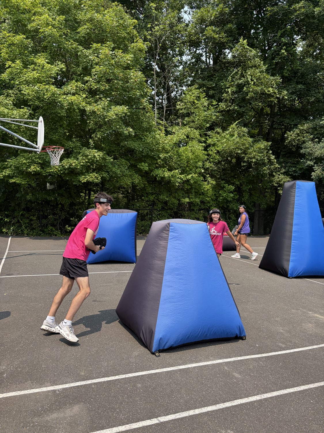Camp participants moving between blue and black pyramid bunkers during an active outdoor laser tag game