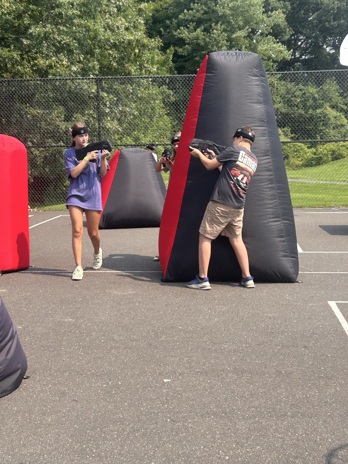 Campers in action behind tall red and black inflatable bunkers on an outdoor court playing Laser Tag On The Go