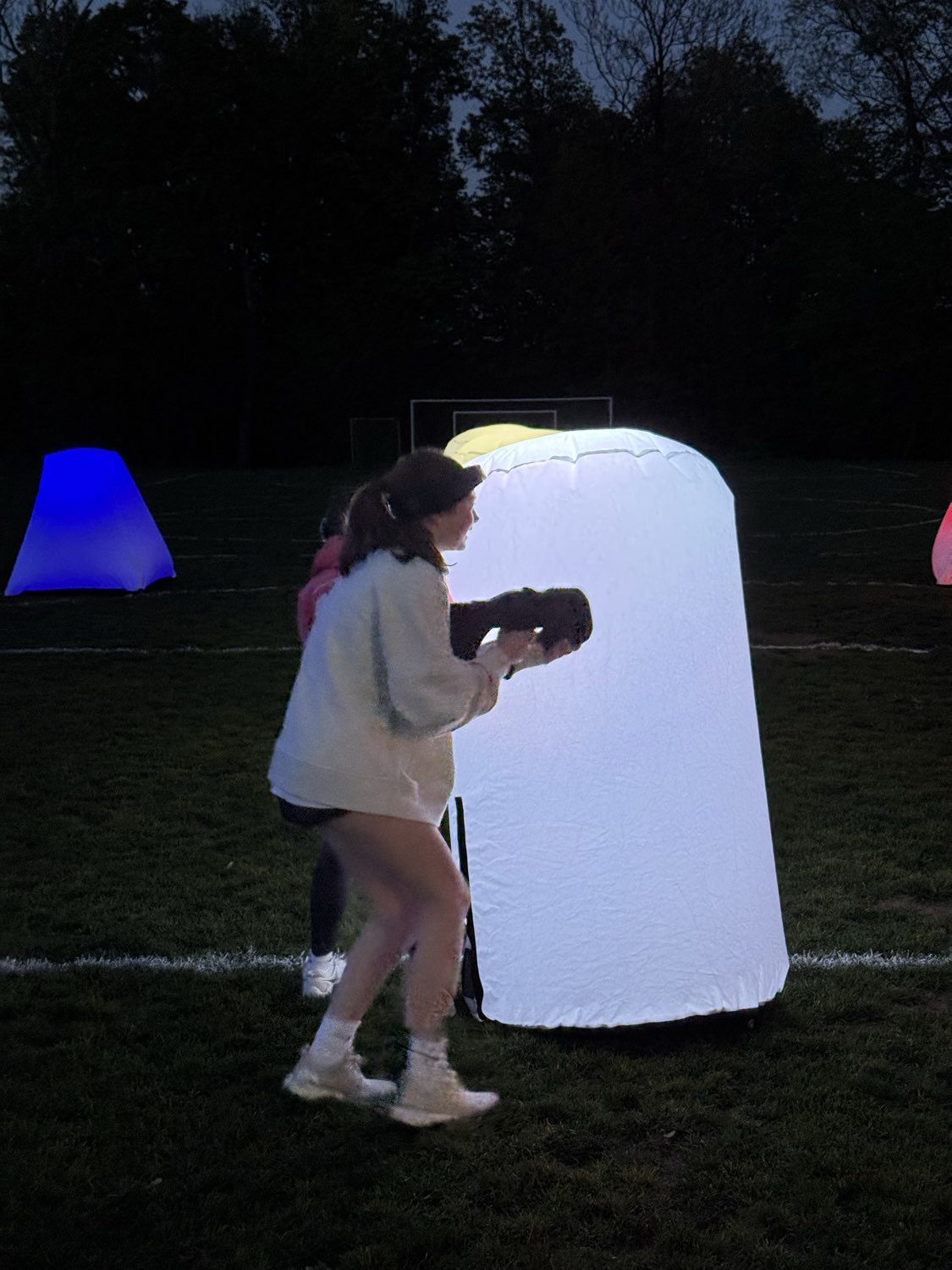 Laser tag player taking cover and aiming from behind an illuminated white bunker on the outdoor Glow Course at night