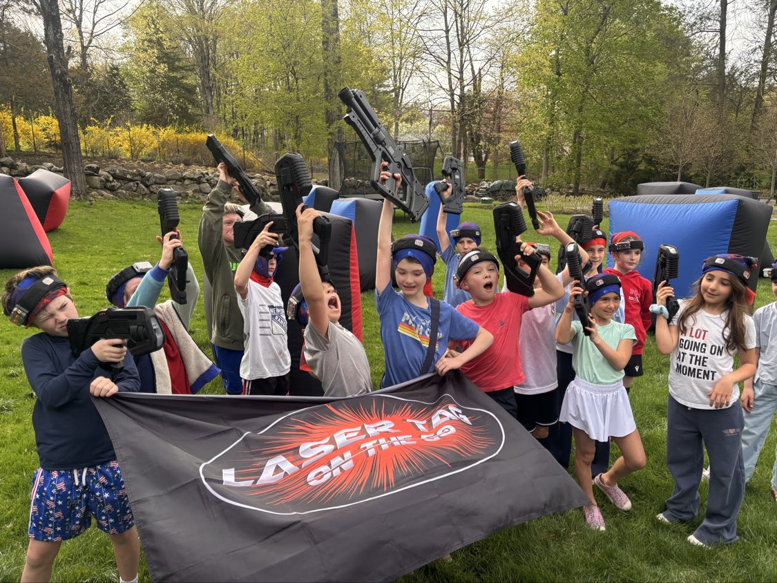 Celebratory birthday party group holding blasters high with the Laser Tag On The Go banner