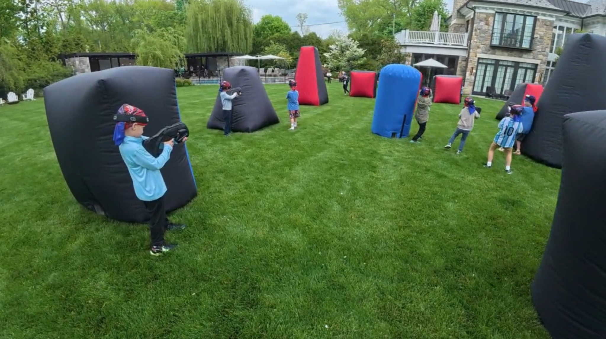 Kids playing an active outdoor mobile laser tag game on an open lawn during a birthday event
