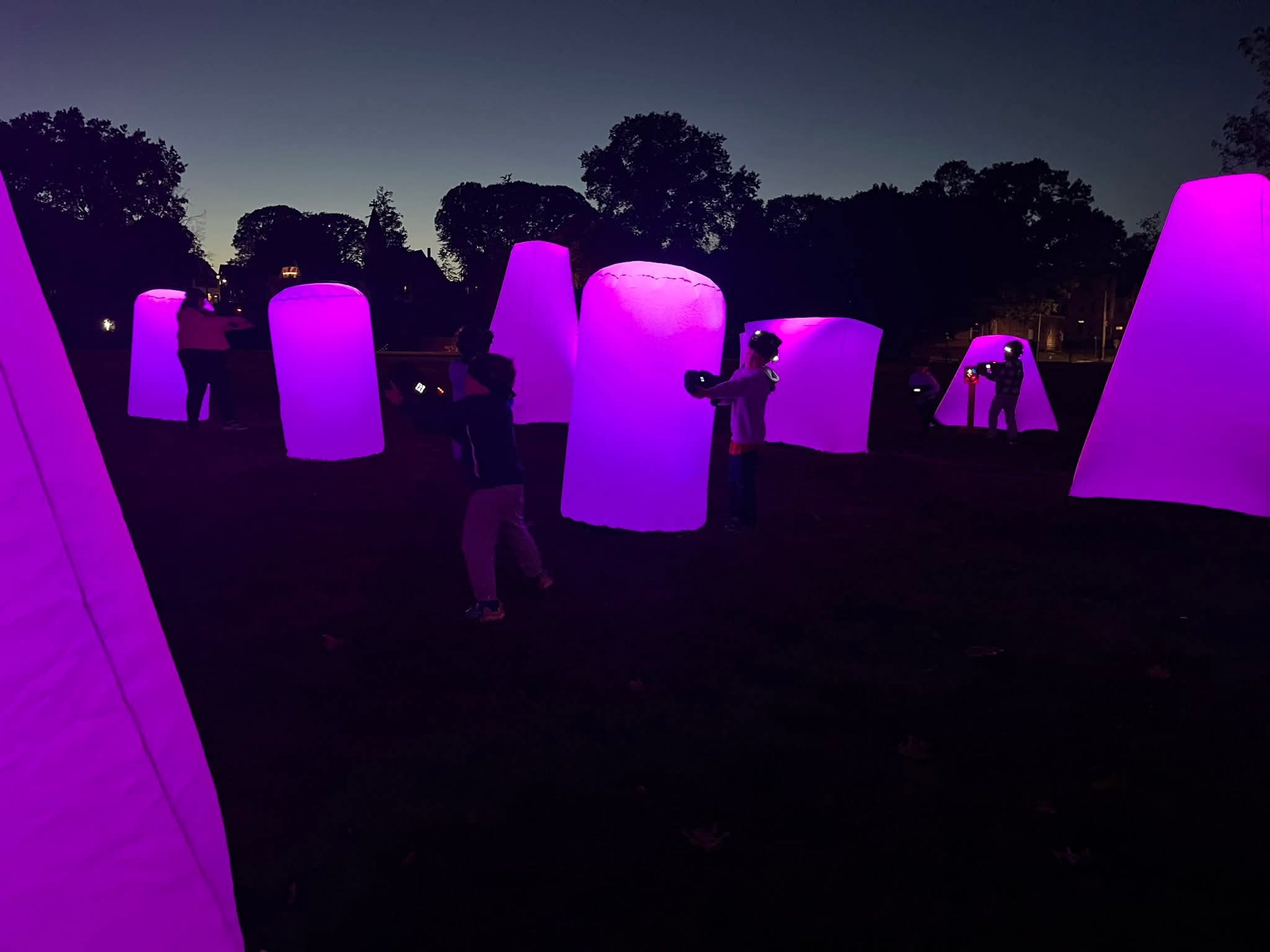 Illuminated Laser Tag Arena — players in action around purple glowing bunkers at night
