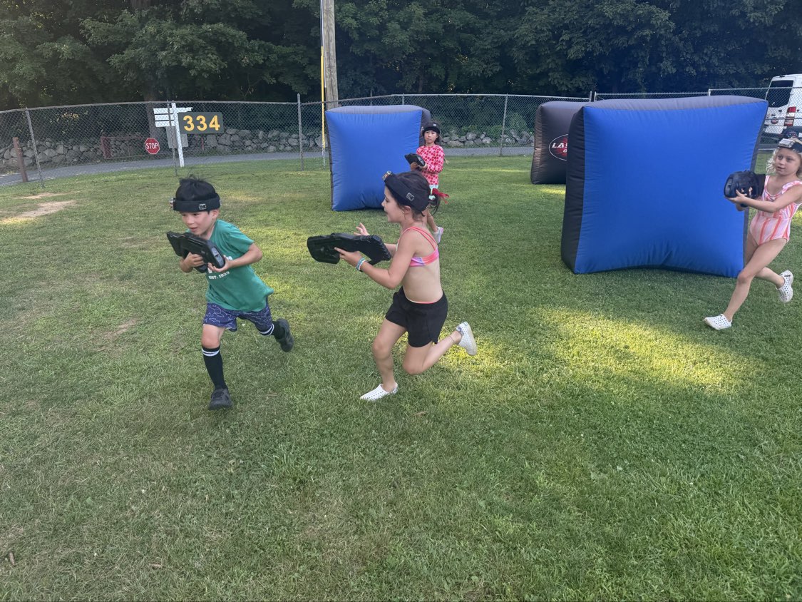Campers running across a grassy field playing Laser Tag On The Go with blasters and headbands