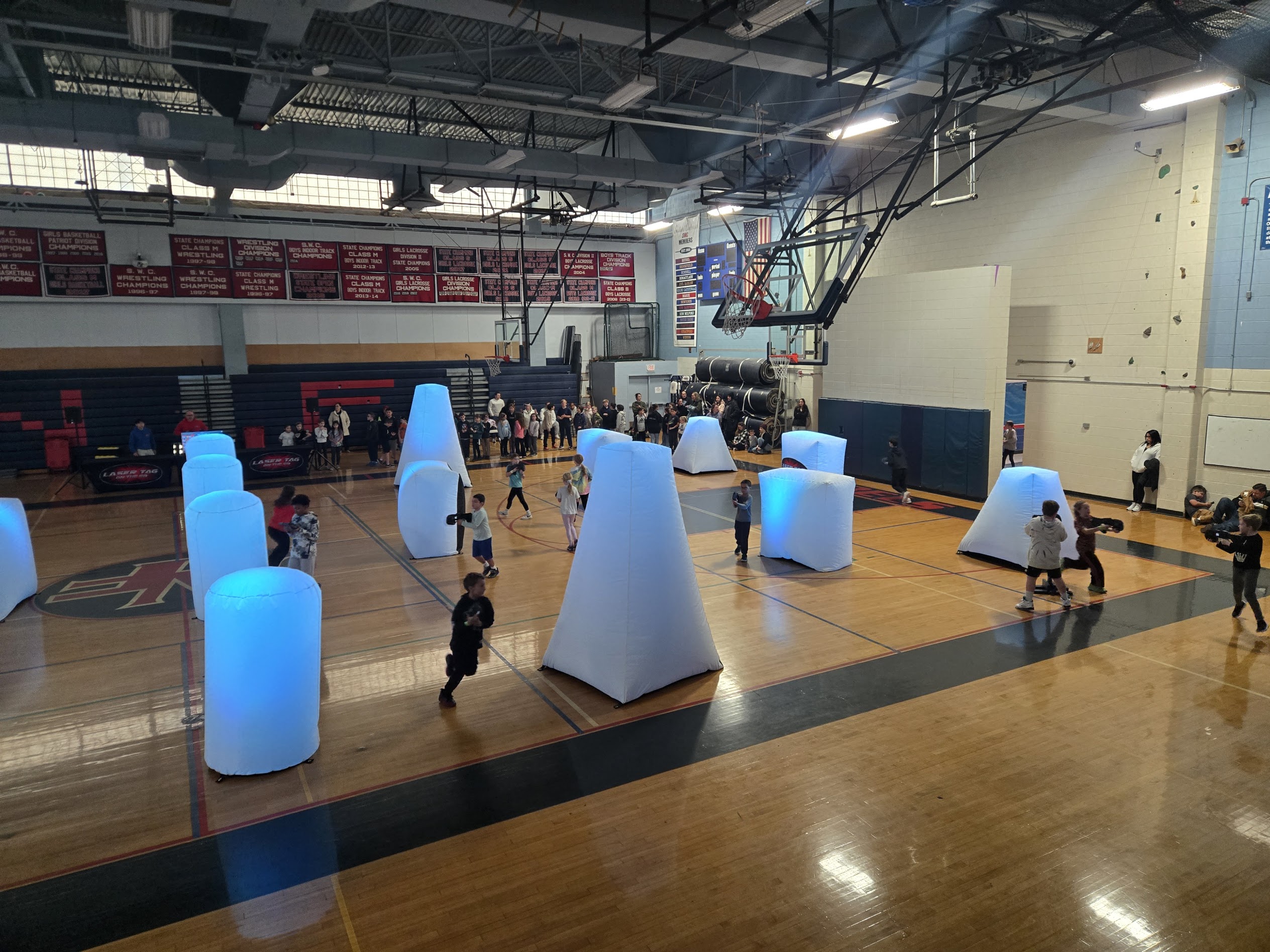 School gym laser tag event with students playing among illuminated white bunkers