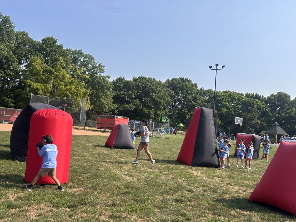 Summer camp players and Game Coach on an open grass field with red and black mobile laser tag bunkers