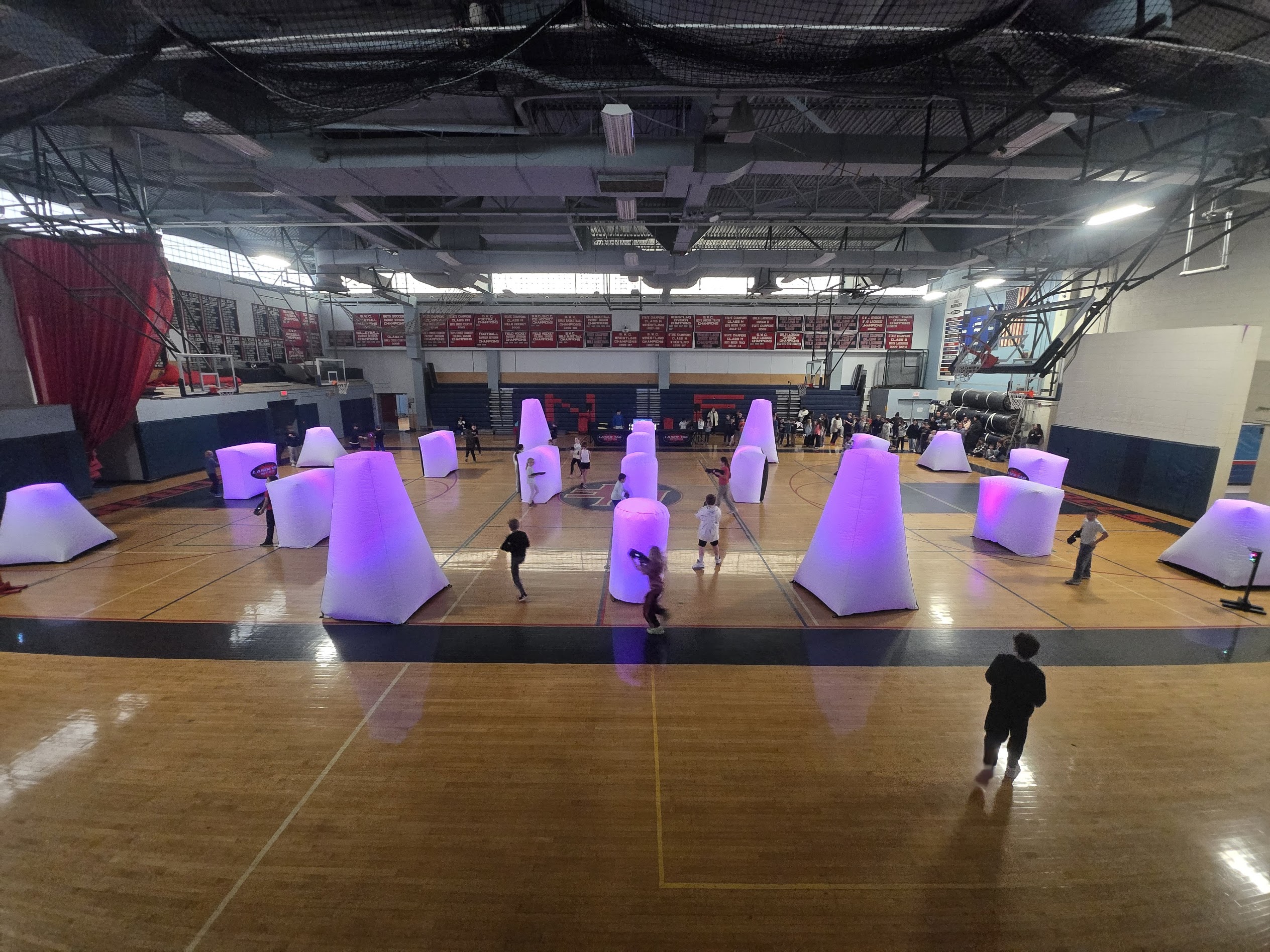 Students playing Laser Tag On The Go in a school gym with illuminated inflatable bunkers