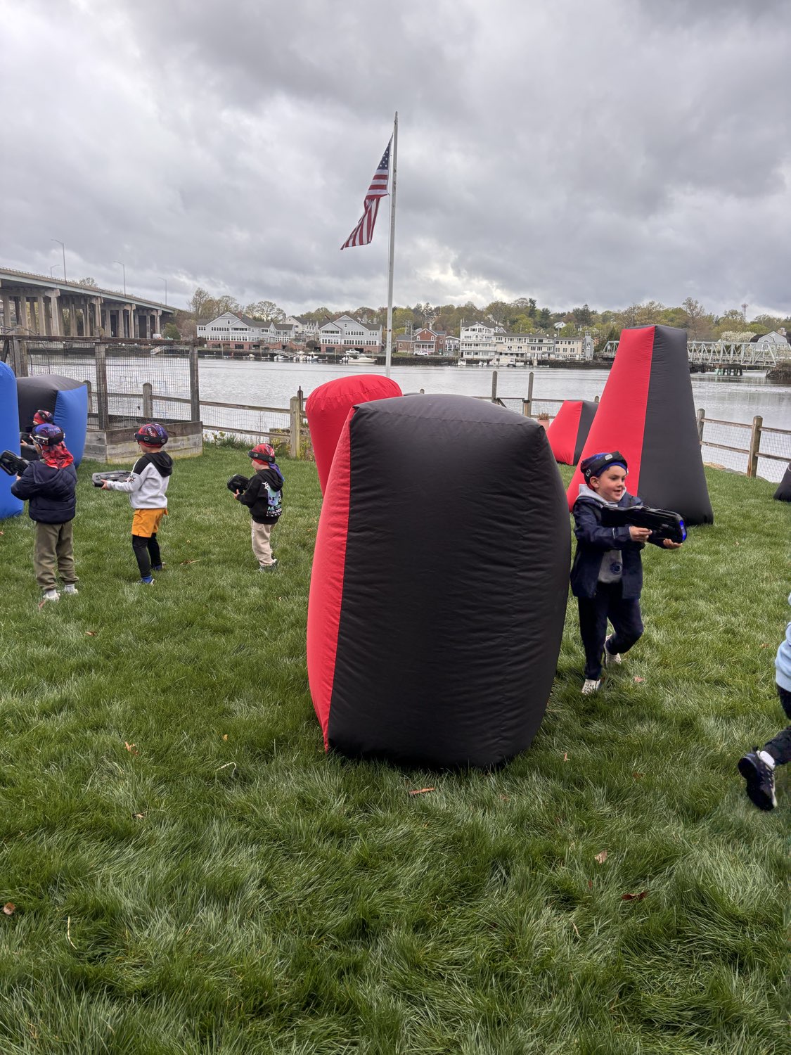 Community laser tag event in action on a scenic waterfront lawn with red and black inflatable bunkers