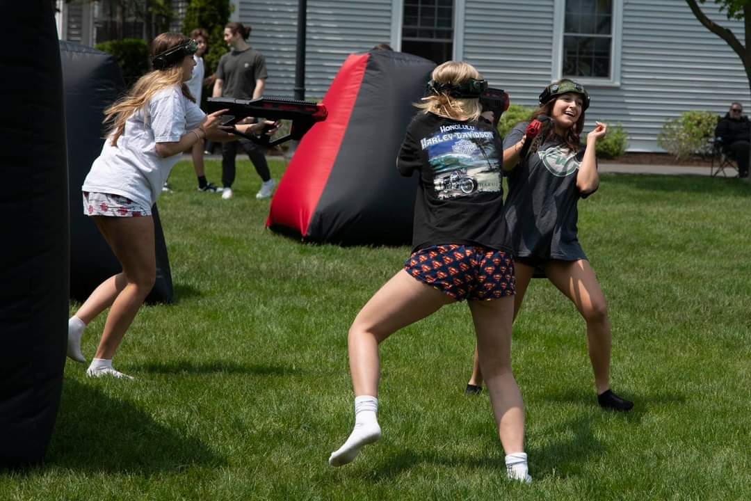 Camp participants having fun in an active mobile laser tag match around inflatable bunkers on an outdoor lawn