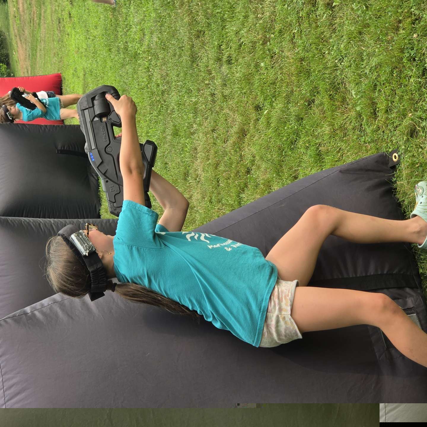 Camp player taking cover and aiming blaster from an inflatable bunker during a summer camp match