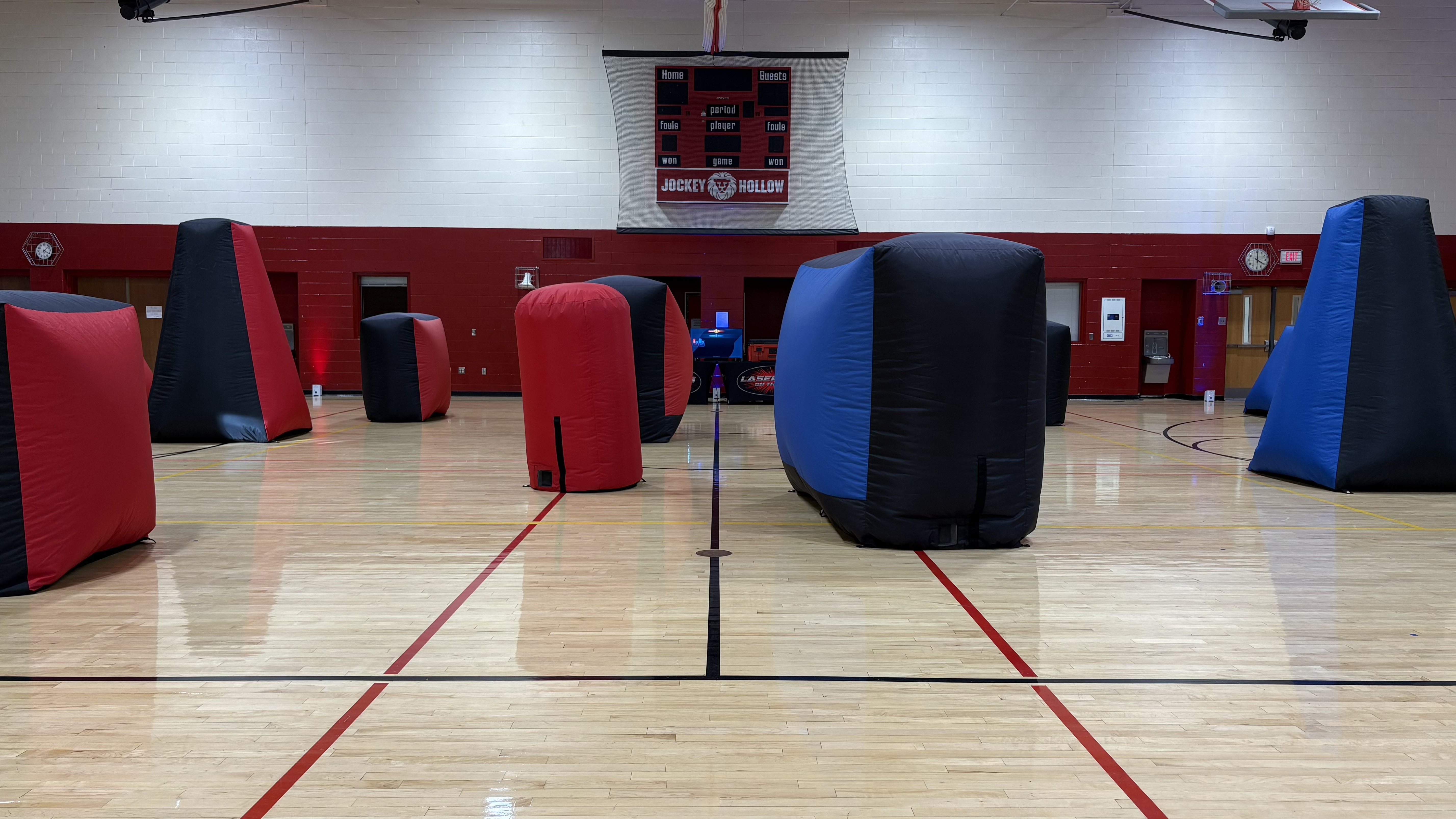Laser Tag On The Go mobile arena setup in a school gymnasium with red and blue inflatable bunkers across the basketball court