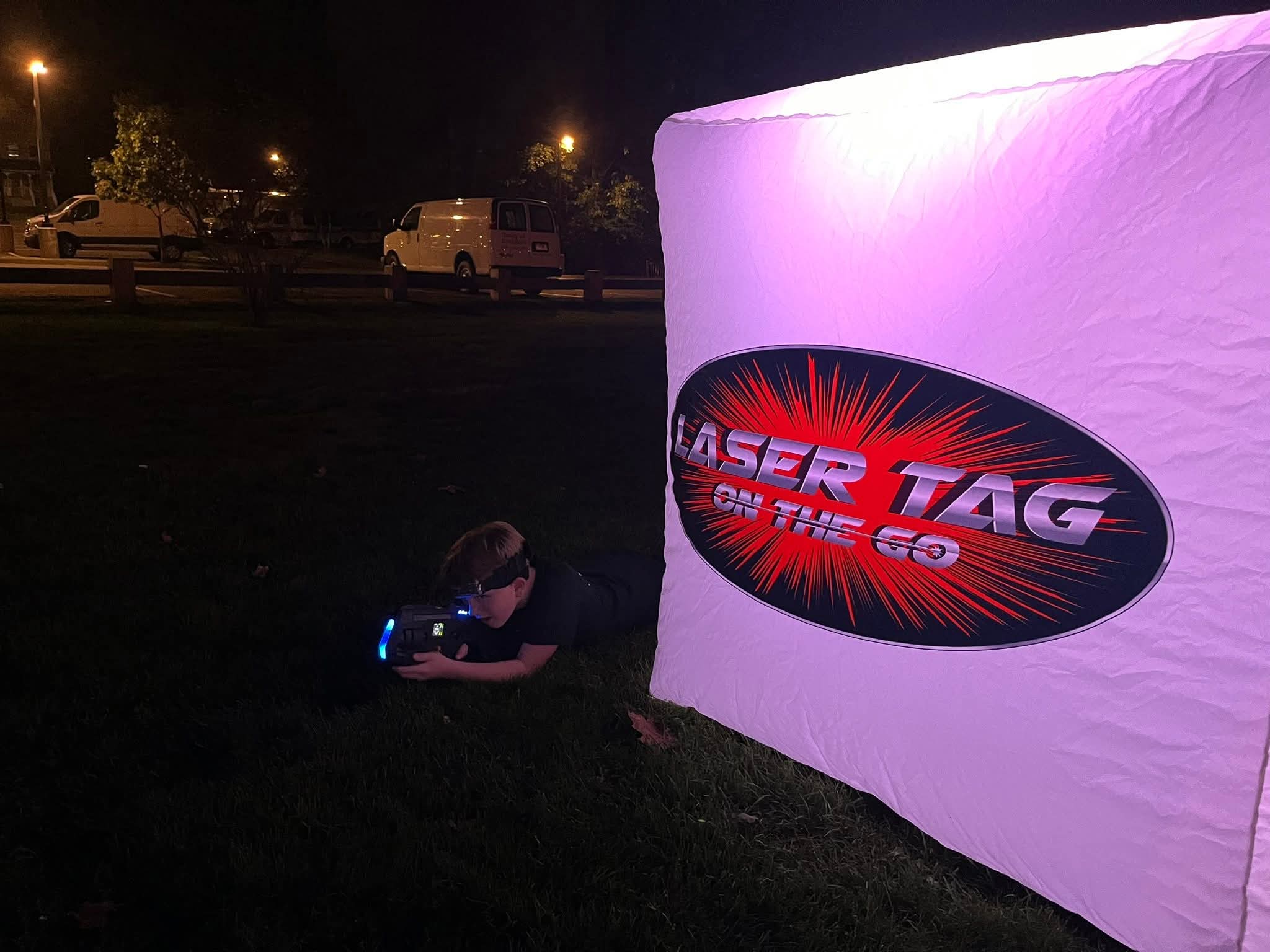 Player beside an illuminated Laser Tag On The Go bunker on the Glow Course at night