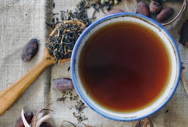 Taza de infusión de té negro Assam con licor rojizo profundo junto a hebras y especias