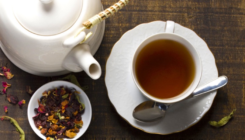 Tetera de cerámica blanca, taza de té servida y hebras aromáticas