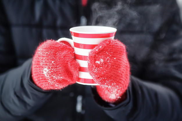 Taza de té caliente sostenida con guantes rojos en pleno invierno para combatir la gripe
